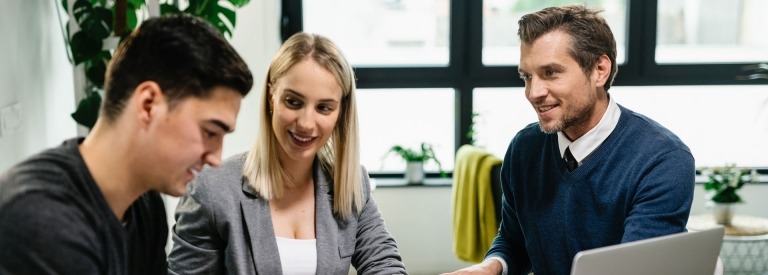 Glimlachende verzekeringsagent die een jong koppel aanbiedt om een contract te ondertekenen tijdens de bijeenkomst.